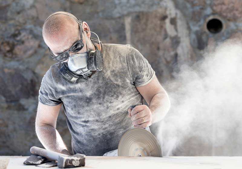 Worker cutting quartz countertop or engineered stone with dust flying.